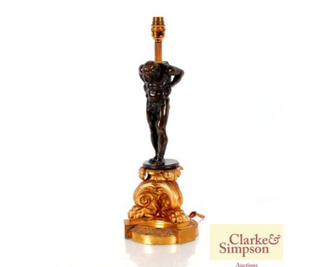 A bronzed and gilded table lamp in the classical manner, decorated with a figure above foliate scrolls and claw feet complete