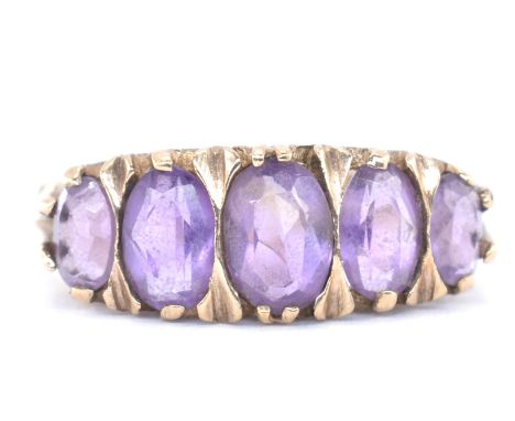 A hallmarked 9ct gold amethyst five stone ring. The ring set with five graduating oval mixed cut amethyst within a gypsy sett