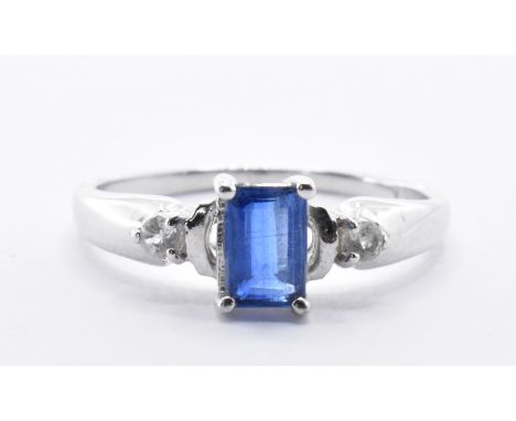 A hallmarked white gold ring being set with a rectangular cut blue stone flanked by two round cut white stones to the shoulde