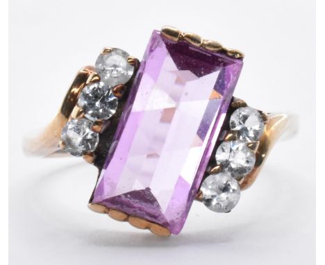 A 9ct gold crossover ring being set with a rectangular fancy cut synthetic pink sapphire flanked with three round cut white s