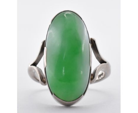 An 18ct white gold and jadeite jade ring having a large oval jadeite cabochon set to split shoulders. Marked 18ct to the band