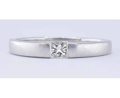 An 18ct white gold band ring being channel set with a square princess cut diamond with textured matte effect shoulders. Marke