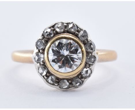 A gold and diamond cluster ring being bezel set with a brilliant cut diamond with a halo of further faceted diamonds. Gold un