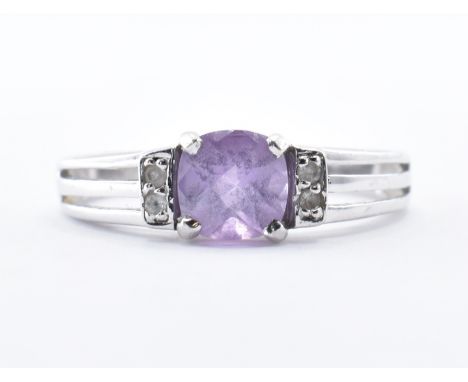 A hallmarked white gold ring being set with a faceted purple stone flanked by four white accent stones with pierced shoulders