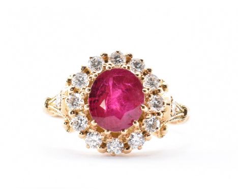 An 18ct gold ruby and diamond cluster ring being set with an oval cut ruby with a halo of of round cut diamonds having scroll