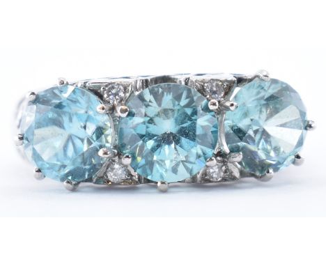 A 9ct white gold three stone ring prong set with three round cut blue zircons with four white accent stones having pierced de