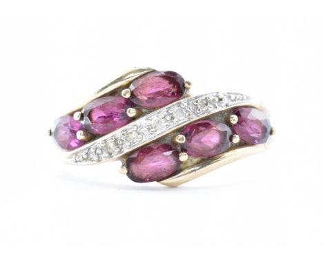 A 9ct gold crossover ring having a central row of diamonds flanked by six faceted purple stones within claw settings. Size O.