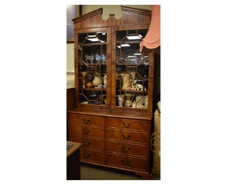 Reproduction mahogany-finish bookcase on cabinet on the Georgian taste, the 'broken' pediment over wooden tracery glazed door