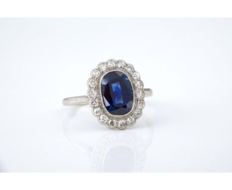 An antique platinum, sapphire and diamond cluster ring, 1920s, the elongated cushion cut sapphire within a scalloped border o