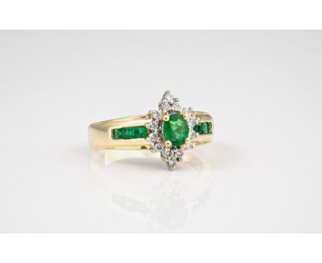 A 14ct gold, emerald and diamond cluster ring, the oval cut emerald within a border of fourteen brilliant cut diamonds, over 