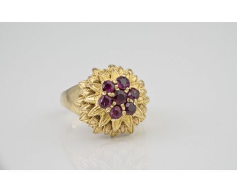 A vintage 9ct yellow gold and garnet cocktail ring, the domed, foliate ring set with a floral cluster of seven round cut garn