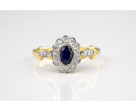 A Victorian style 18ct yellow gold, sapphire and diamond cluster ring, the oval cut sapphire within a scalloped border of bri