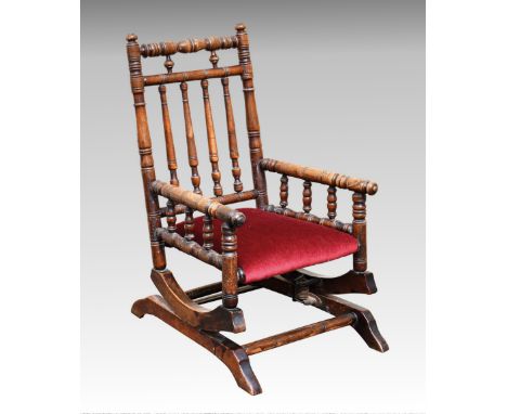 A late Victorian sprung base child's rocking chair, the beechwood bobbin turned frame over a dark red velvet stuff over seat,