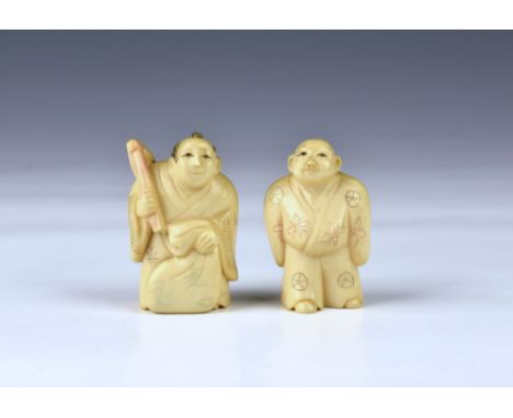 A pair of Japanese ivory netsukes, of figures in traditional dress, both having red character marks to underside, the tallest