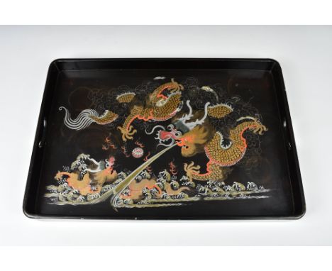 A Chinese lacquered dragon tray, 1920s-30s, black lacquer with two pierced handles, boldly painted with two dragons chasing a