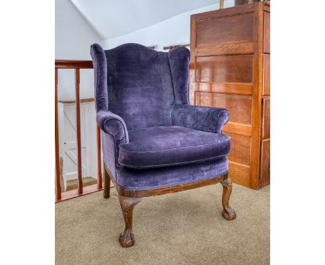 An early 20th century Georgian style wing armchair, with amethyst upholstery, on cabriole legs with carved shells to the knee