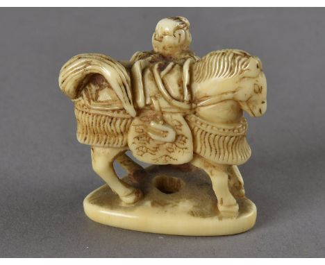 A Japanese ivory netsuke, modelled as a horse and groom with an ornate decorative saddle and bridle on a triangular base, uns