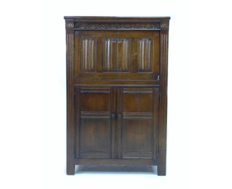 A mid 20th century dark stained oak drinks cabinet, in Old Charm style, applied linenfold decoration to the fall front, openi