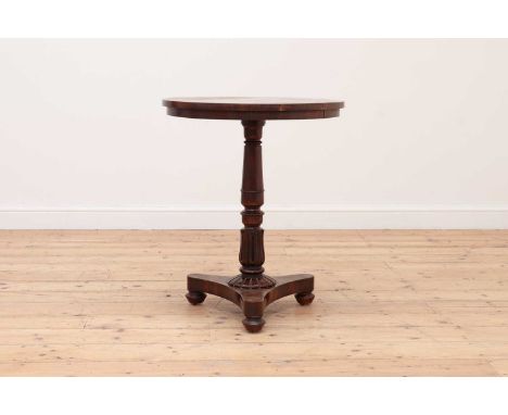 An early Victorian rosewood lamp table,the circular top on a turned column with carved stylised stiff leaves and a triform ba