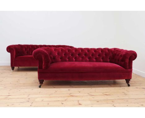 A matched pair of Victorian chesterfield sofas,each button upholstered, in a dark pink velvet, on turned front legs and casto