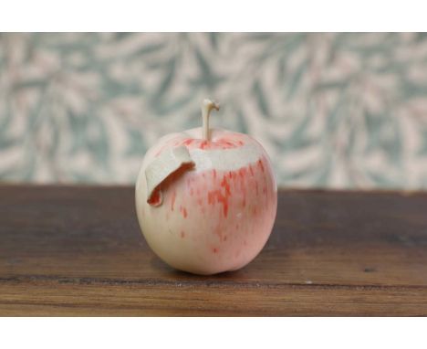 A carved and stained ivory okimono,Meiji period (1868-1912), Japanese, in the form of an apple with partially-peeled skin, 6c