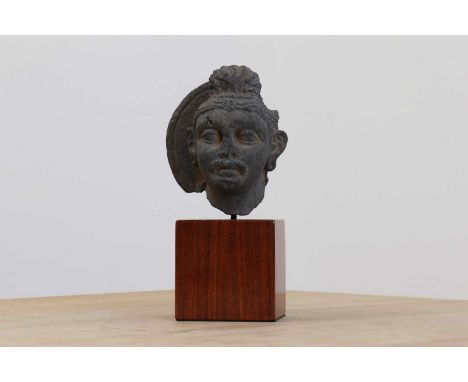 A carved schist fragmentary head of a bodhisattva,Gandhara, on a modern wooden plinth,11cm wide7.5cm deep20cm highCondition r