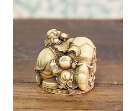 An ivory netsuke,Meiji period (1868-1912), Japanese, of a recumbent elephant lying on a circular plinth, with two boys clambe