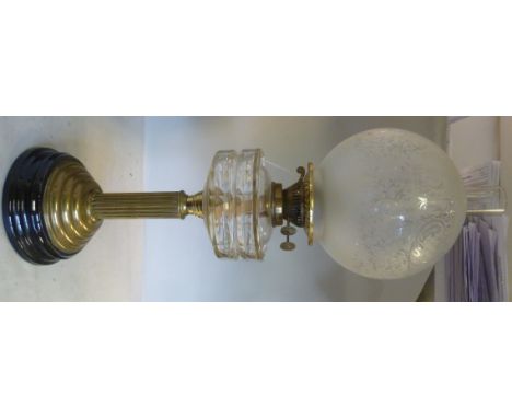 An early 20thC oil lamp, the brass burner set in a clear, facet cut glass reservoir, on a reeded brass column, the stepped ba