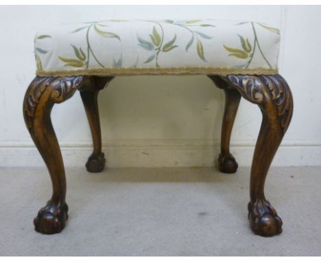 A 1920s George II inspired stool, having a green floral and beige upholstered top, raised on mahogany cabriole legs with acan