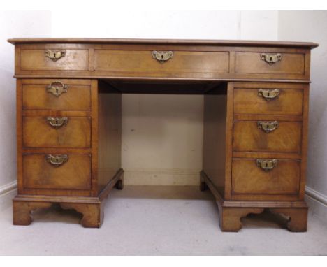 An early 20thC Queen Anne inspired walnut desk, having a tooled brown hide scriber, over three in-line drawers and twin pedes