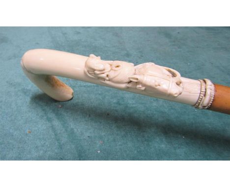 A late 19c walking cane with white bone handle carved with a harnessed horses head and a gun dog with cartridge bag and powde