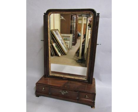 A George III figured mahogany toilet glass with gilt border, adjustable and supported on base with fitted three short drawers
