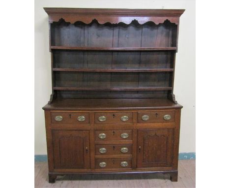 An early 18c English oak three drawer dresser with a panel back rack having three open shelves under a moulded cornice with s