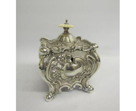 A late Victorian tea caddy of square embossed design with scroll work and flowers and supported on four feet.  The hinged cov