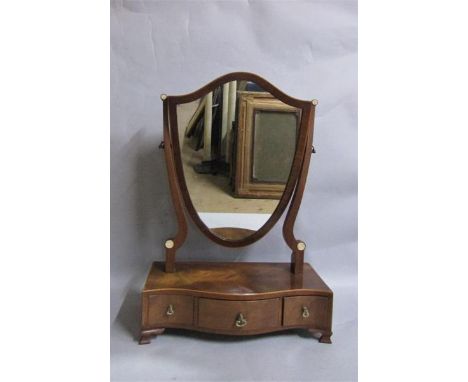 A late Georgian mahogany shield shaped toilet glass on a serpentine base fitted three short drawers with ogee bracket feet.  