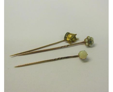 A collection of three gold stick pins, one set with Emerald and Seed Pearl, one set Opal, the other with Dog head terminal.  