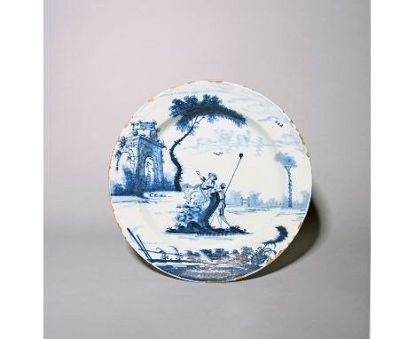 A London delftware charger  c.1770, painted in blue with a maiden reclining on a rocky outcrop and attended by a young shephe