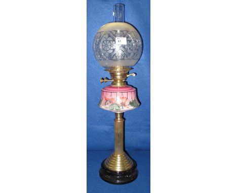 Early 20th Century brass double burner oil lamp with floral decorated ceramic reservoir on a brass pedestal and ceramic base.
