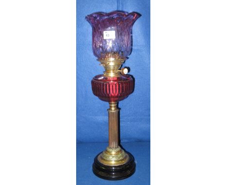 Early 20th Century double burner oil lamp with cranberry glass reservoir on a fluted brass column with ceramic base, graduate