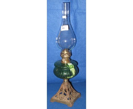 Brass single burner oil lamp with coloured glass reservoir, cast metal base and clear chimney.