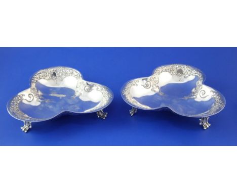 A pair of early 20th century silver trefoil shaped bonbon dishes, with embossed foliate scroll border, on three pierced scrol