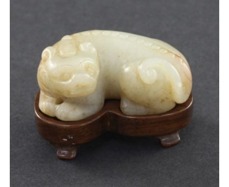 A Chinese pale celadon and russet jade recumbent figure of a bixi, 19th century, 5cm, wood stand