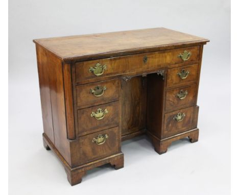 A George II walnut and crossbanded kneehole desk, fitted with central recessed cupboard door and an arrangement of seven draw