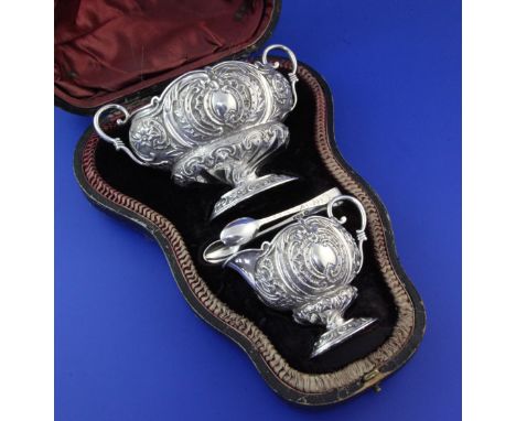 A cased late Victorian silver cream and sugar set with tongs, of oval form, embossed with foliate scrolls, John Round & Sons,