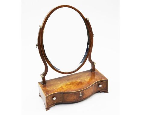 A George III mahogany and rosewood crossbanded oval toilet mirror, the serpentine base fitted with three drawers, on bracket 