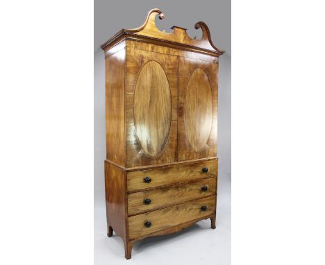 A George III mahogany linen press, with swan neck pediment above two cupboard doors, with central oval panels, enclosing five
