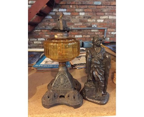 A RESIN FIGURINE OF AN ANGLER 24CM TALL AND A VINTAGE CAST LAMP WITH AMBER COLOURED GLASS RESERVOIR 