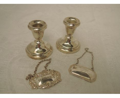 A pair of small HM silver candle sticks of squat form having weighted bases and two HM silver decanter labels including whisk
