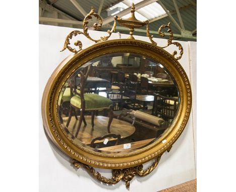 Gilt composition wall mirror, oval bevelled plate, urn and scroll surmount, width 85cm.