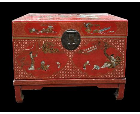 A Chinese lacquered trunk on stand decorated with figures and flowers, on a red ground, 68cms wide.